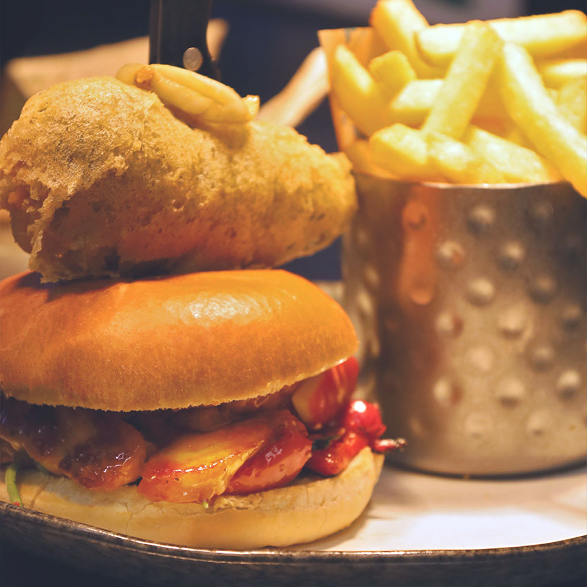 Halloumi burger served at ICE restaurant in Bury St Edmunds, Suffolk, featuring grilled halloumi, roasted peppers and chutney in a brioche bun, topped with a crispy onion ring and served with chunky chips.